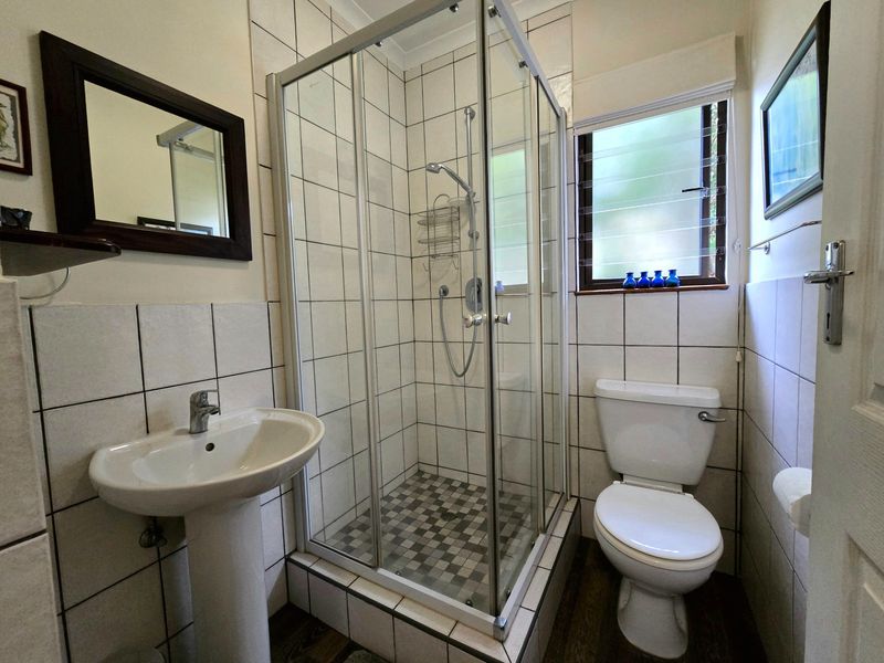 A functional bathroom featuring a pedestal basin, a glass-enclosed shower, and a standard toilet, finished with neutral wall tiling.