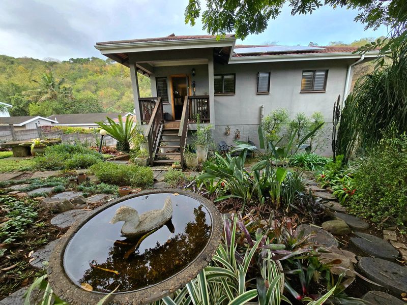 A view of the rear elevation featuring a covered timber deck, staircase access, and a well-established landscaped garden with stone pathways.