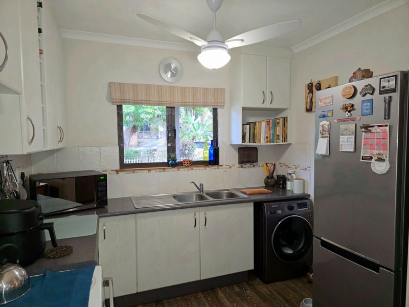 A functional kitchen featuring laminate countertops, a double sink, tiled backsplash, and built-in cabinetry with an integrated laundry appliance space.