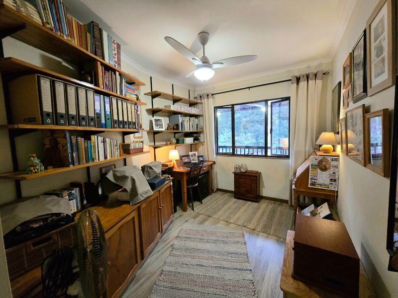 A functional home office featuring built-in wall shelving, a ceiling fan, and a window providing natural light.