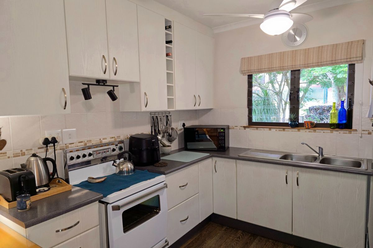 A functional kitchen featuring white cabinetry, laminate countertops, a stainless steel double sink, and a freestanding stove with a tiled backsplash.
