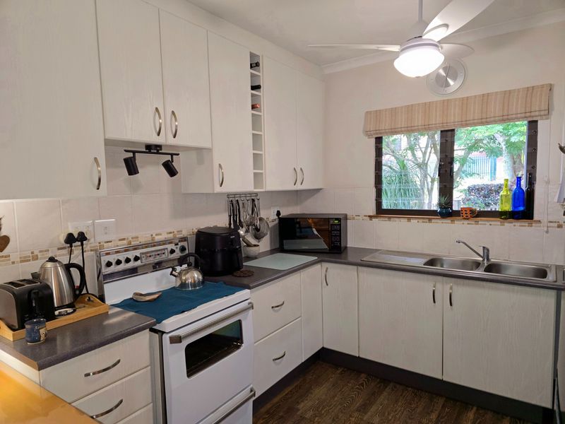 A functional kitchen featuring white cabinetry, laminate countertops, a stainless steel double sink, and a freestanding stove with a tiled backsplash.