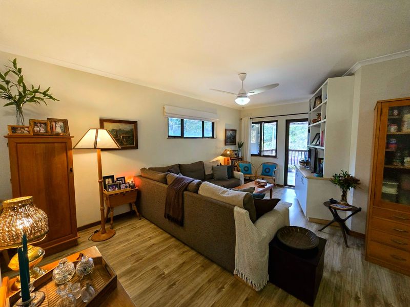 A comfortable living room featuring laminate flooring, a ceiling fan, and a built-in shelving unit, with direct access to an outdoor balcony area.
