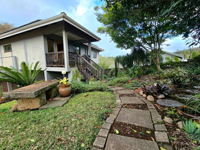 A rear garden view featuring a raised wooden deck, stone paved pathway, and established landscaping with a stone bench.