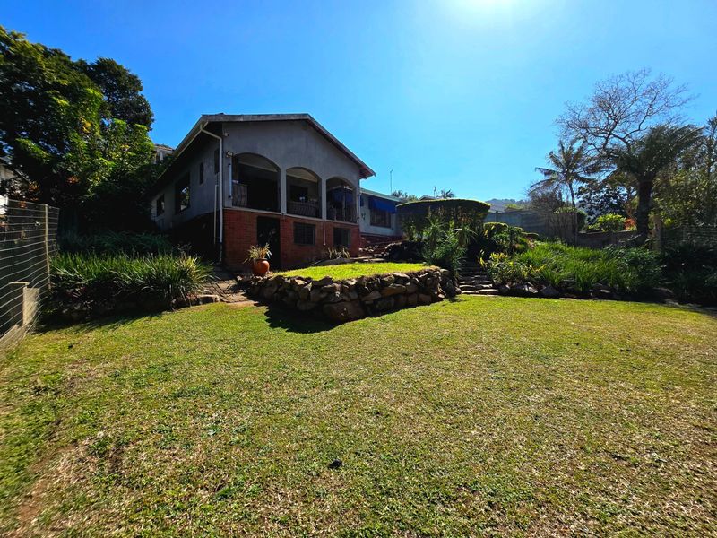 A view of the rear elevation featuring a covered patio, stone retaining wall, and a well-maintained garden area.
