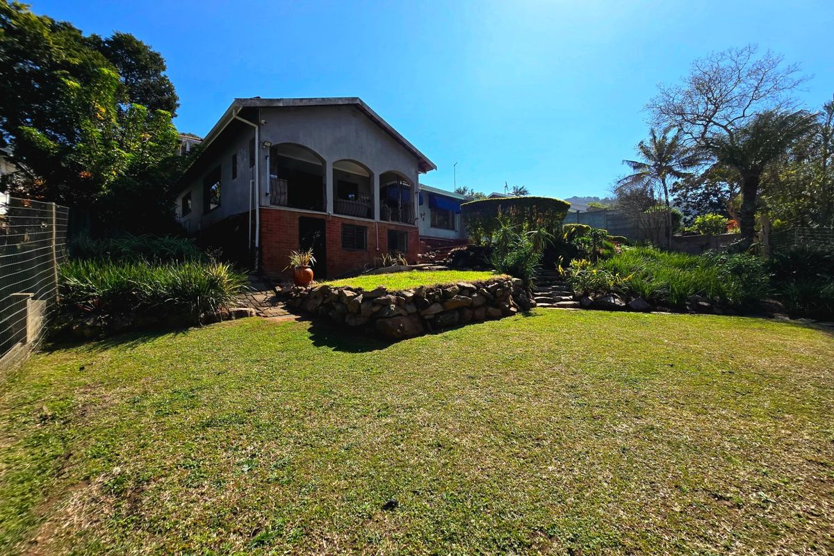A view of the rear elevation featuring a covered patio, stone retaining wall, and a well-maintained garden area.