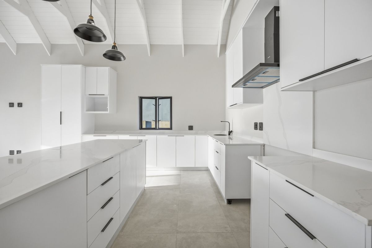 Modern, minimalist kitchen featuring white cabinetry, quartz countertops, a central island, and a vaulted ceiling with pendant lighting.