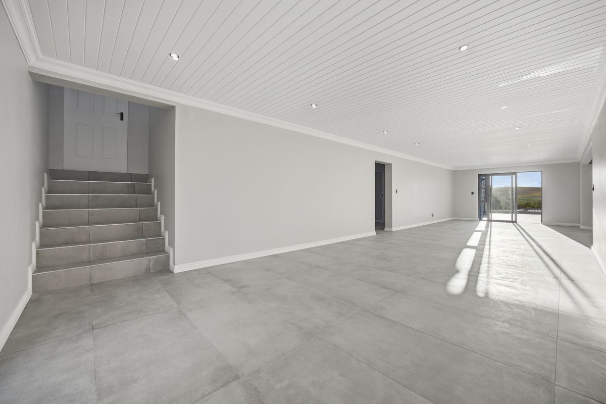 A spacious, empty living area featuring modern grey floor tiles, a white tongue and groove ceiling with recessed lighting, and access to an outdoor area.