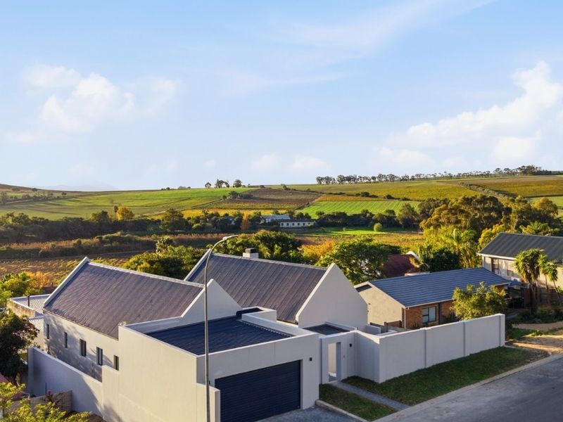 Aerial view of a modern residential property featuring a pitched roof, integrated garage, and boundary wall, set against a scenic rural landscape.