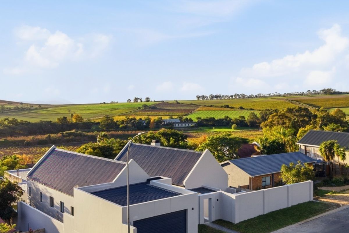 Aerial view of a modern residential property featuring a pitched roof, integrated garage, and boundary wall, set against a scenic rural landscape.