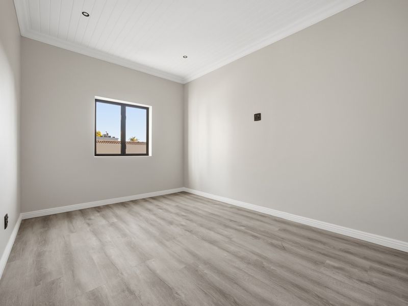 A bright, empty bedroom featuring modern laminate flooring, a tongue and groove ceiling with recessed lighting, and neutral wall finishes.