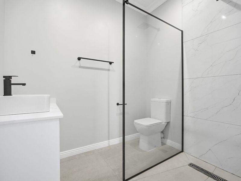 Modern bathroom featuring a walk-in shower with black-framed glass screen, marble-look wall tiles, vessel sink, and contemporary black tapware.