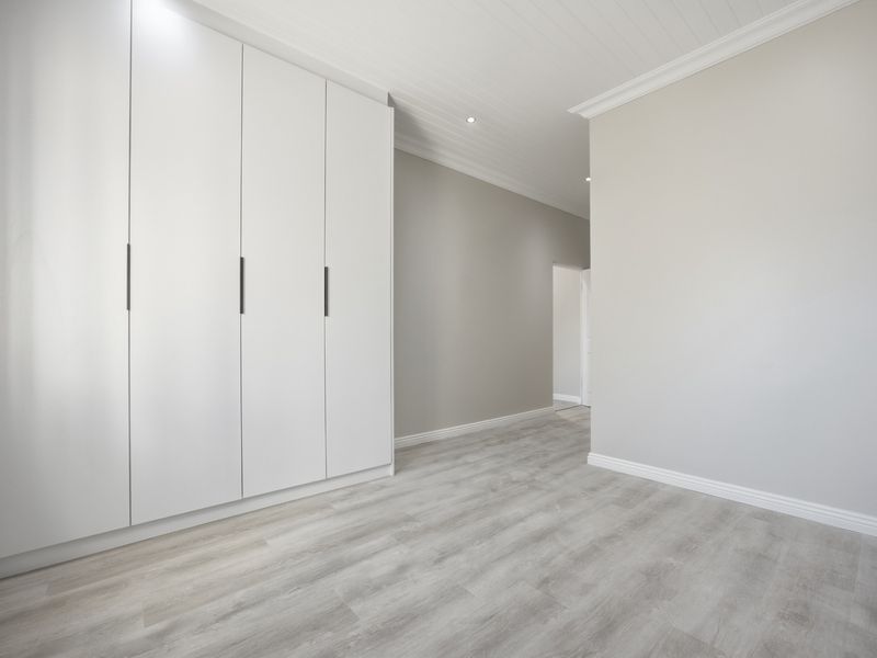 A bright, modern bedroom featuring neutral walls, light laminate flooring, built-in cupboards, and a classic tongue and groove ceiling.