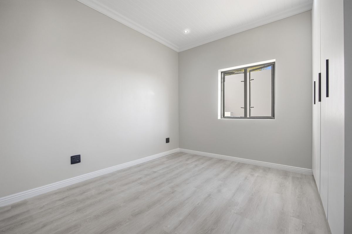 A bright, neutral bedroom featuring modern laminate flooring, built-in cupboards, and clean finishes, offering a versatile space ready for personalization.