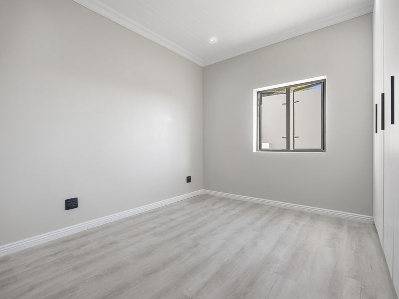 A bright, neutral bedroom featuring modern laminate flooring, built-in cupboards, and clean finishes, offering a versatile space ready for personalization.