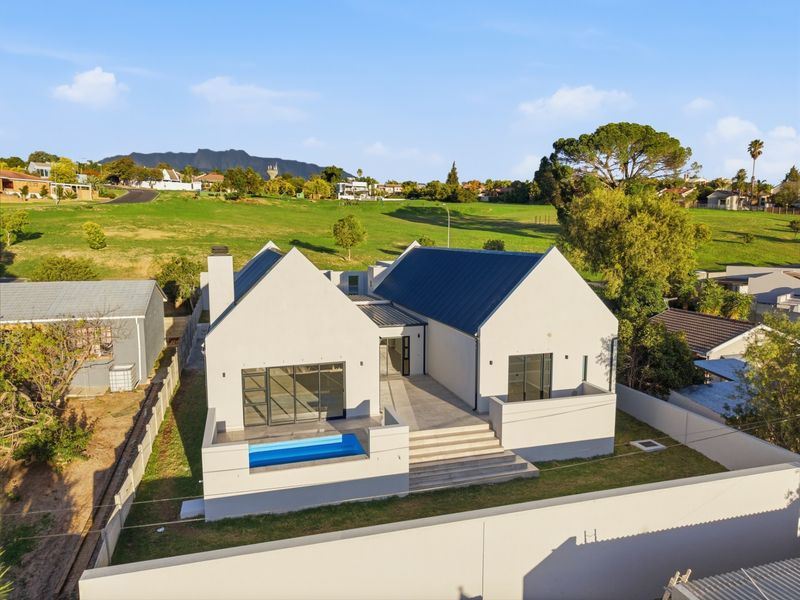 Aerial view of a modern house featuring a metal roof, a swimming pool, and a spacious patio area set against a scenic landscape.