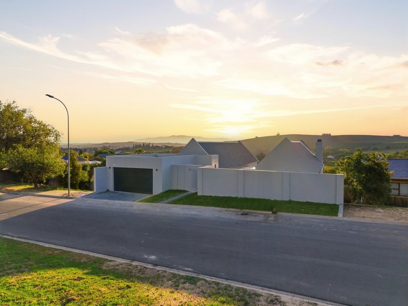A modern residential property featuring a clean facade, integrated garage, and boundary wall, set against a scenic landscape at sunset.
