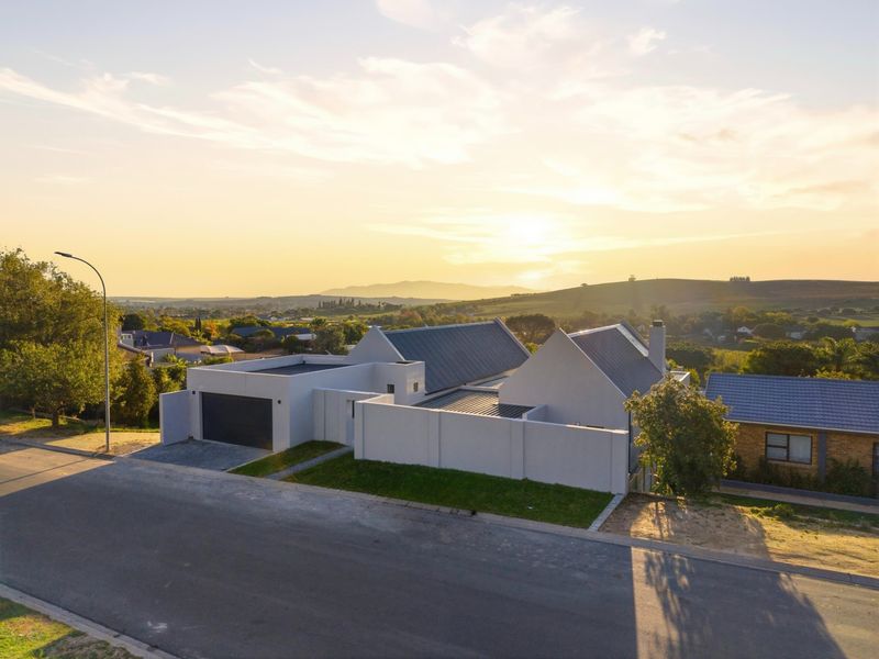 Aerial view of a modern residential property featuring a metal roof, secure boundary walls, and a paved driveway at sunset.