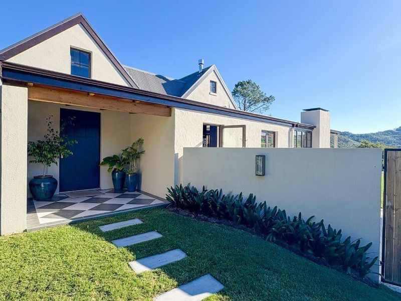 A well-maintained front entrance featuring a covered porch with checkered tiling, a modern boundary wall, and a neat landscaped garden path.