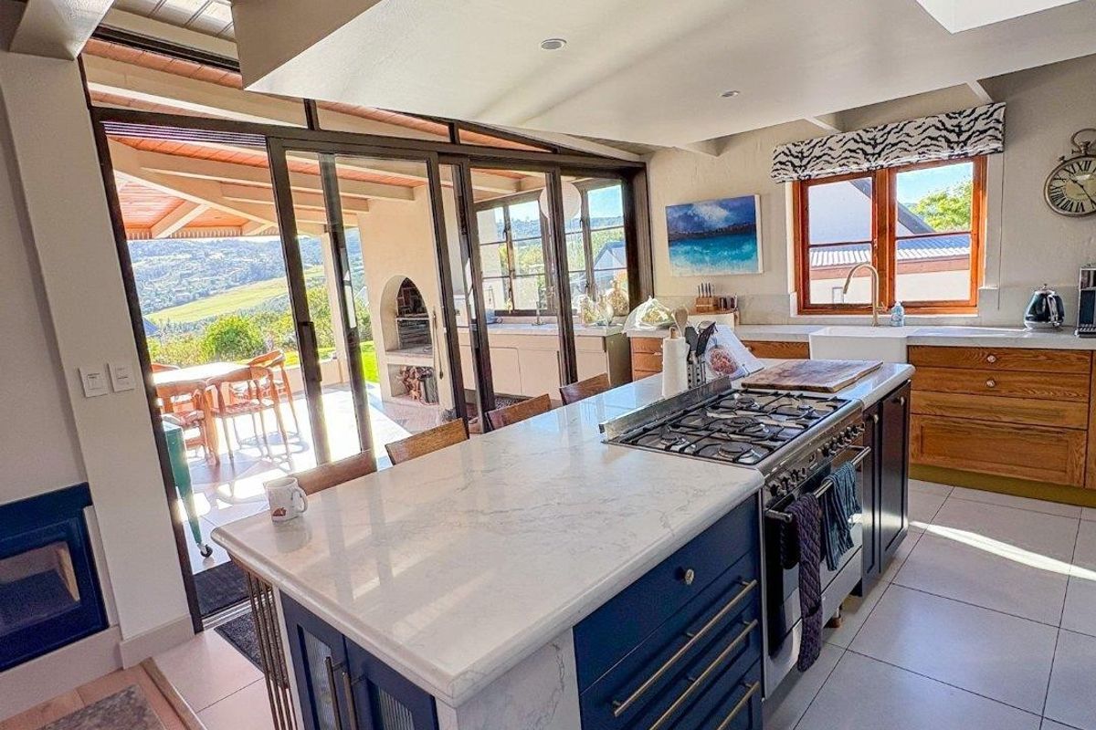 Modern kitchen featuring a large island with gas cooktop, stone countertops, farmhouse sink, and skylight, seamlessly connecting to an outdoor patio area.