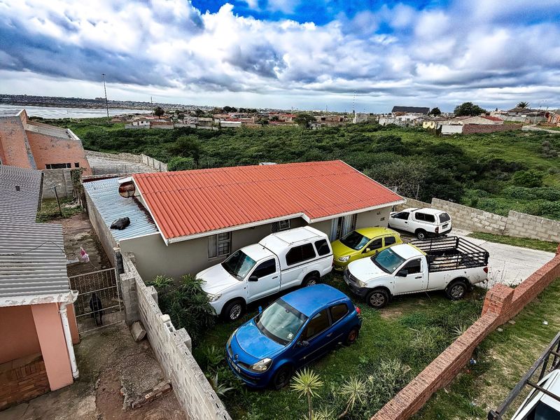Aerial view of a residential property featuring a corrugated metal roof, concrete block boundary walls, and a paved driveway area.