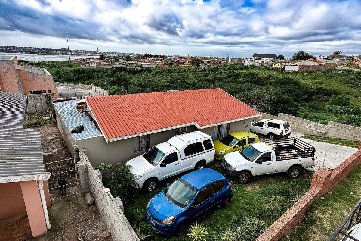 Aerial view of a residential property featuring a corrugated metal roof, concrete block boundary walls, and a paved driveway area.