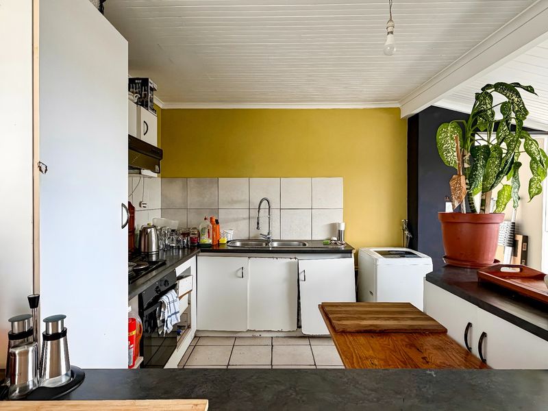 A functional kitchen featuring built-in cabinetry, a stainless steel sink, tiled splashback, and integrated oven and hob, with a bright yellow accent wall.