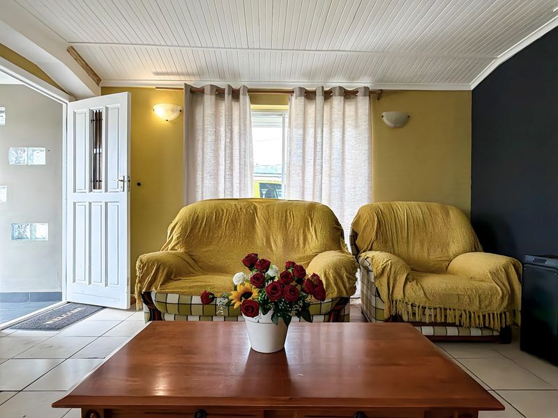A living room featuring tiled flooring, a beaded timber ceiling, and direct access to the exterior through a panelled entrance door.