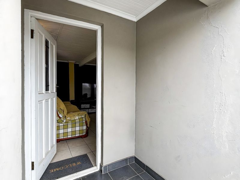 Entrance area featuring tiled flooring and a panelled door, showing signs of wear on the wall plaster.