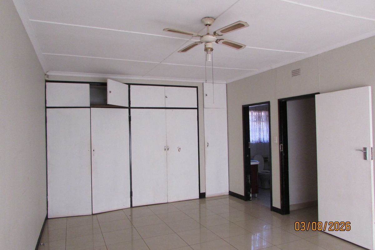A spacious bedroom featuring tiled flooring, a ceiling fan, and extensive built-in cupboard storage with direct access to an adjoining bathroom.