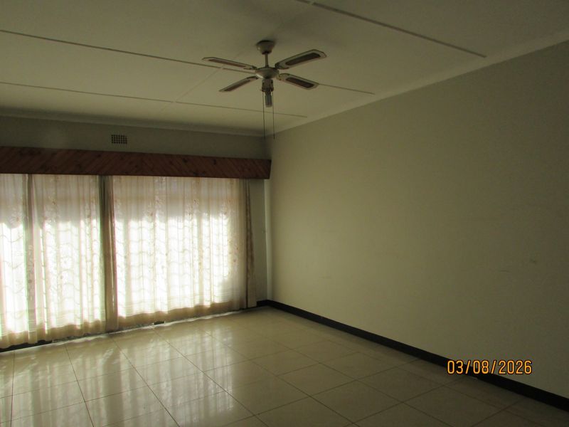 An empty living room featuring tiled flooring, a ceiling fan, and a timber pelmet above the window area.