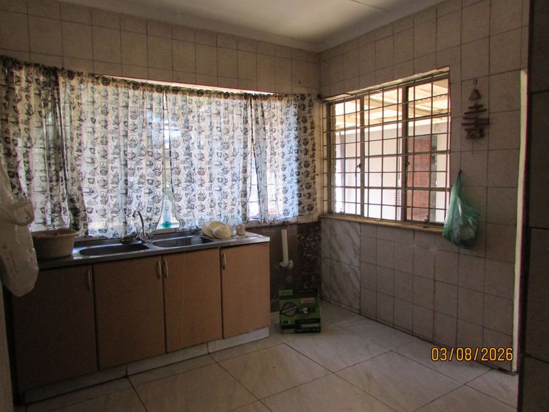A dated kitchen featuring tiled walls, floor tiles, security bars on windows, and a double sink with built-in cabinetry.