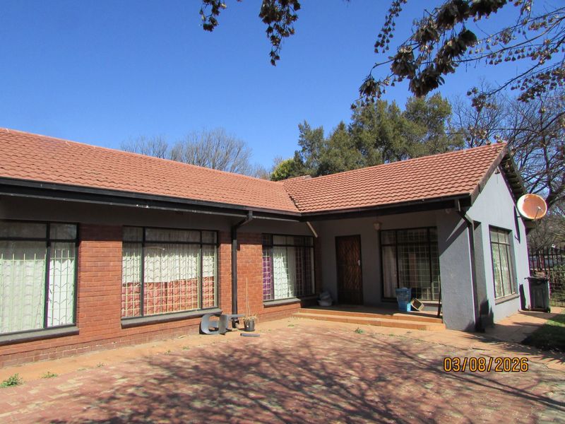 Front elevation of a single-story brick house featuring a tiled roof, paved driveway, and covered entrance area with security bars on windows.