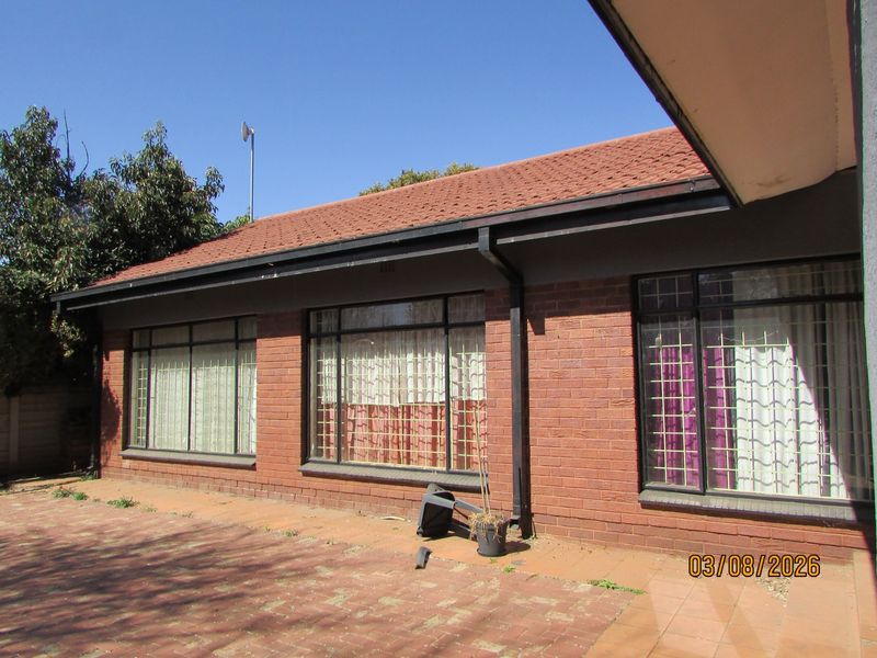 Rear exterior view of a brick house featuring a paved patio area, tiled roof, and windows fitted with security bars.