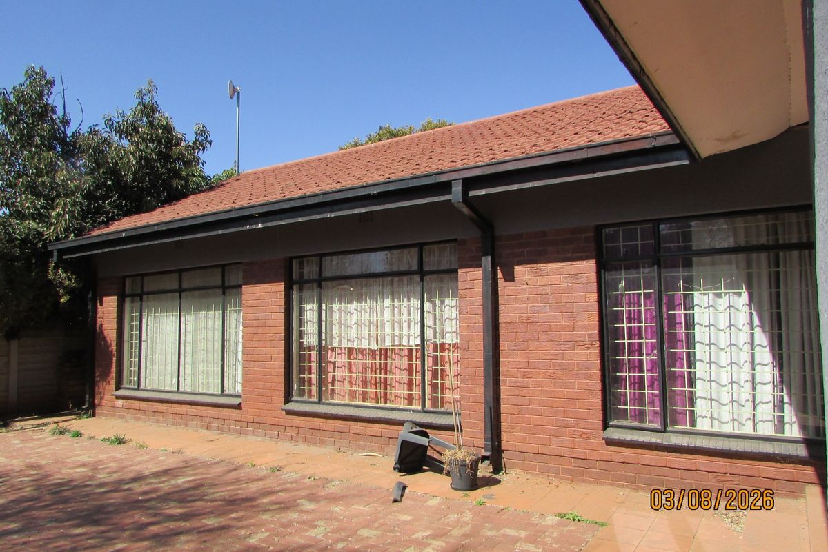 Rear exterior view of a brick house featuring a paved patio area, tiled roof, and windows fitted with security bars.