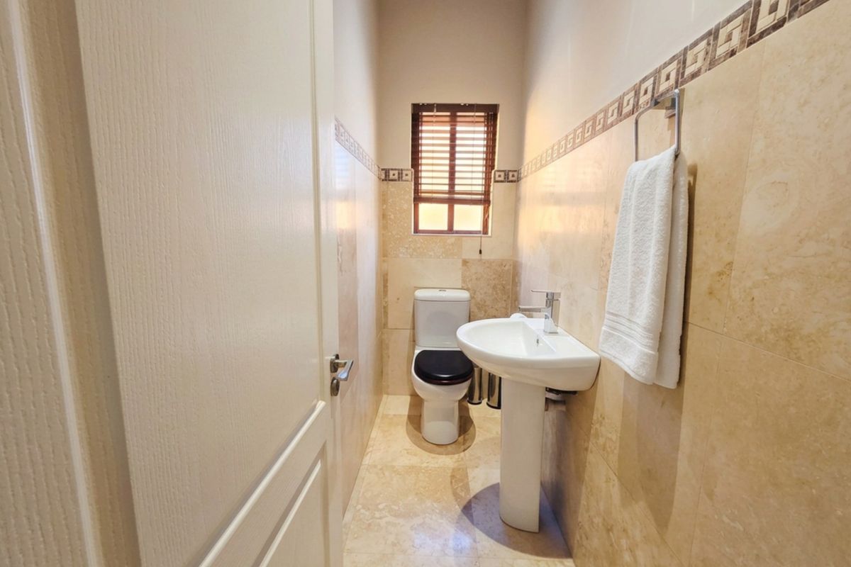 A clean and well-maintained guest bathroom featuring a pedestal basin, toilet, and neutral floor-to-ceiling wall tiling.