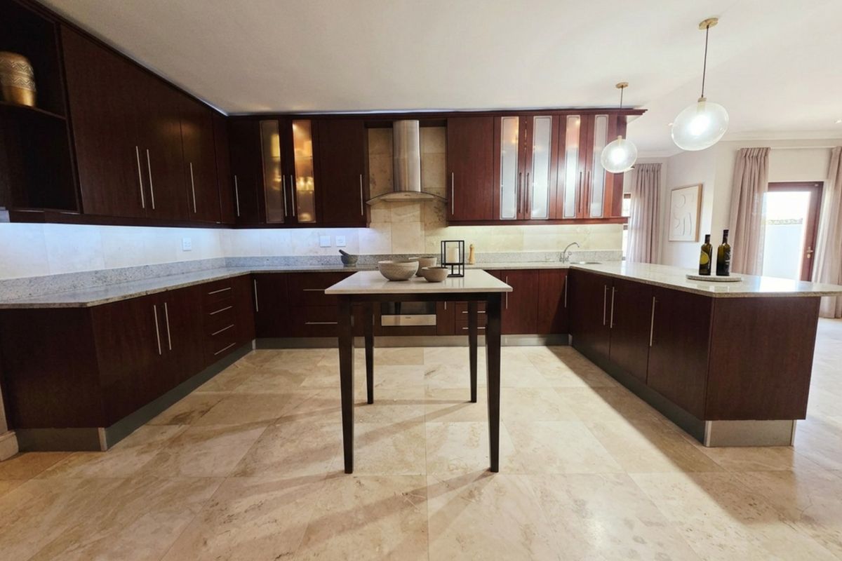 Spacious kitchen featuring dark wood cabinetry, granite countertops, stainless steel extractor fan, and elegant travertine flooring with modern pendant lighting.