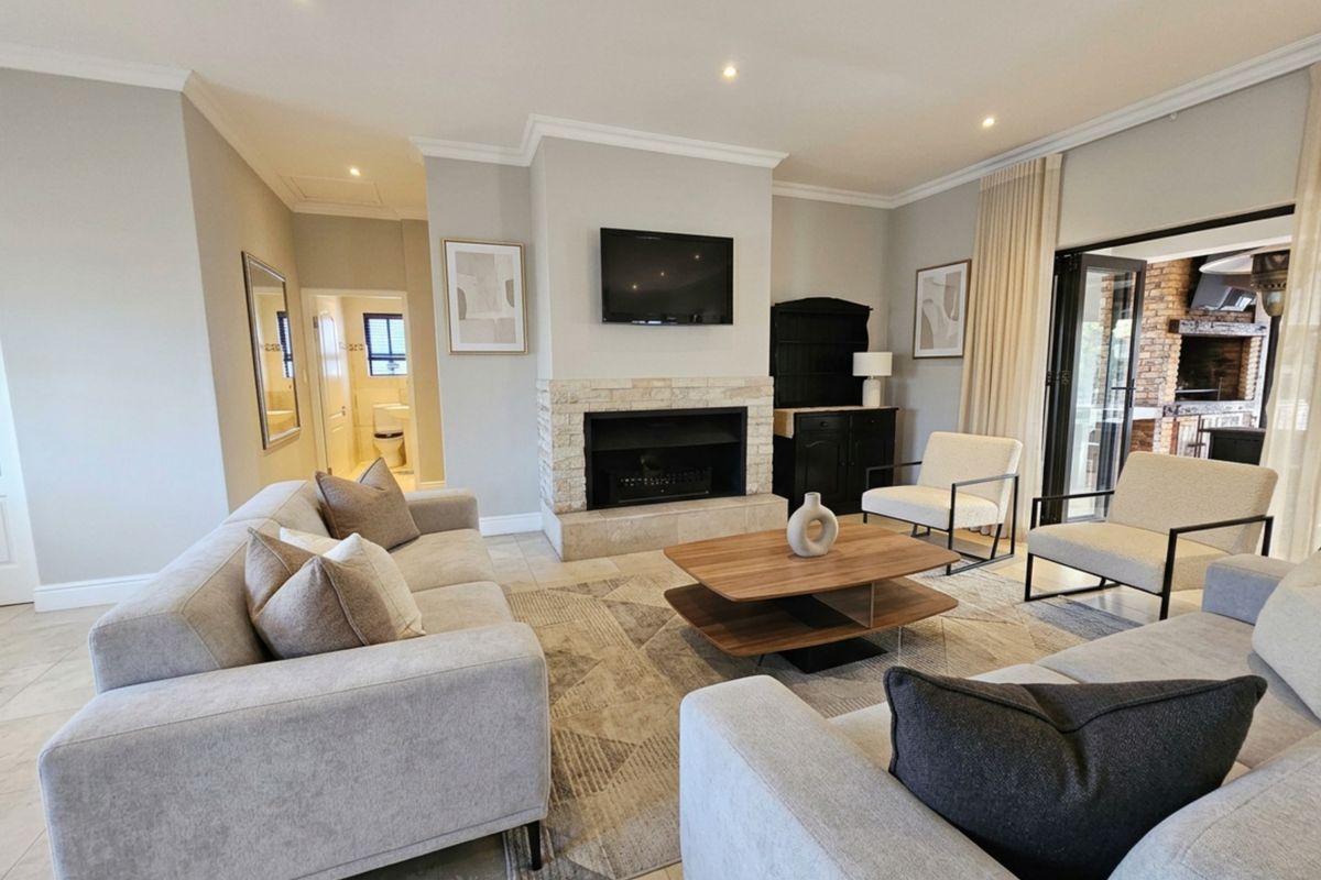 A well-maintained living room featuring a stone-clad fireplace, tiled flooring, and large stacking doors that provide seamless access to the outdoor patio area.