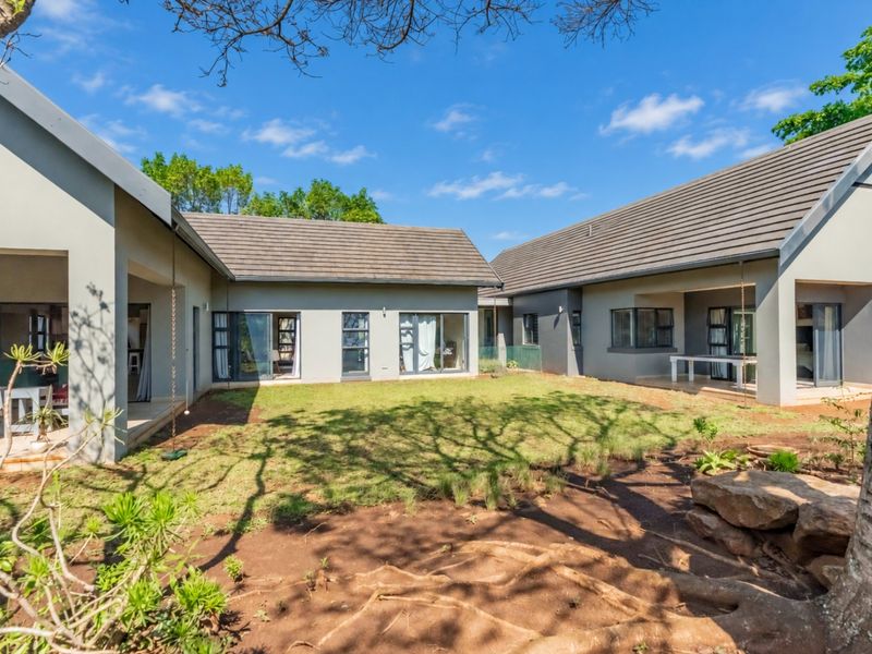 A spacious rear exterior view featuring a well-maintained garden, covered patio areas, and modern architectural design with large sliding doors.