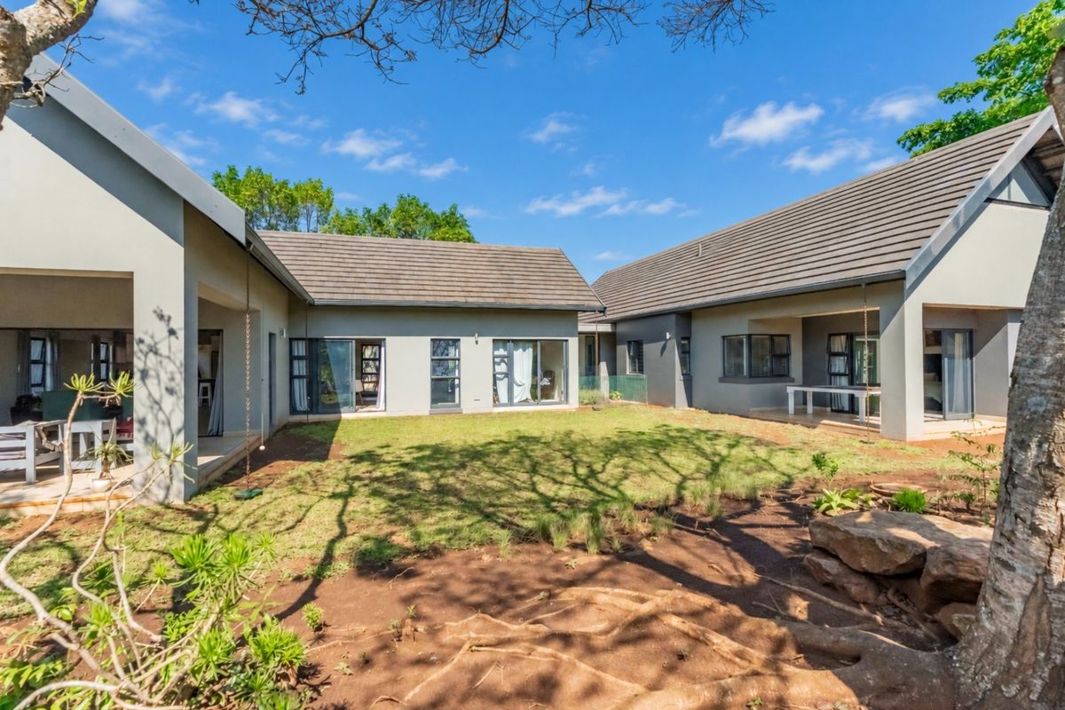 A spacious rear exterior view featuring a well-maintained garden, covered patio areas, and modern architectural design with large sliding doors.