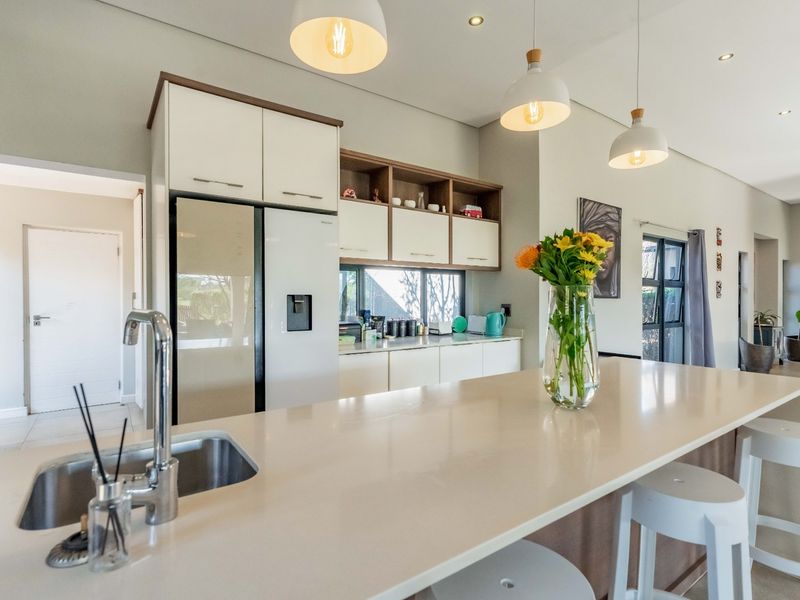 Modern kitchen featuring a large island with quartz countertops, undermount sink, sleek cabinetry, and stylish pendant lighting in an open-plan layout.