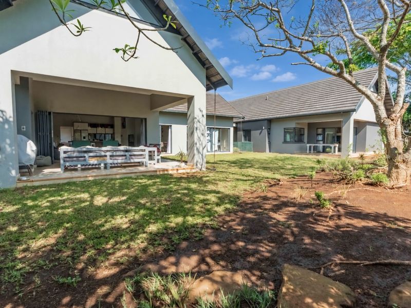 Rear view of the property featuring a covered patio, tiled roof, and a spacious garden area with mature trees.