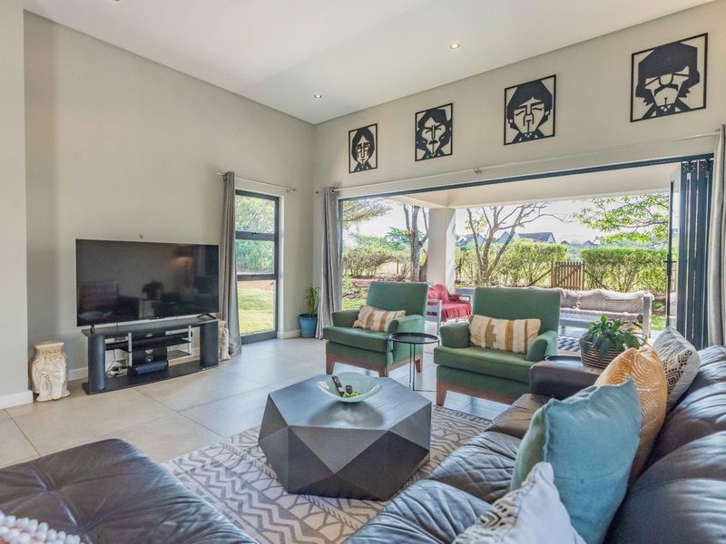 Spacious living room featuring large format floor tiles, recessed lighting, and expansive stacking glass doors that open onto a covered patio and garden.