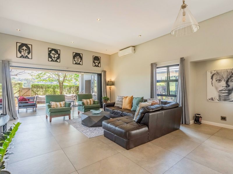 Spacious living room featuring large format floor tiles, recessed lighting, and wide stacking glass doors that open onto an outdoor patio area.