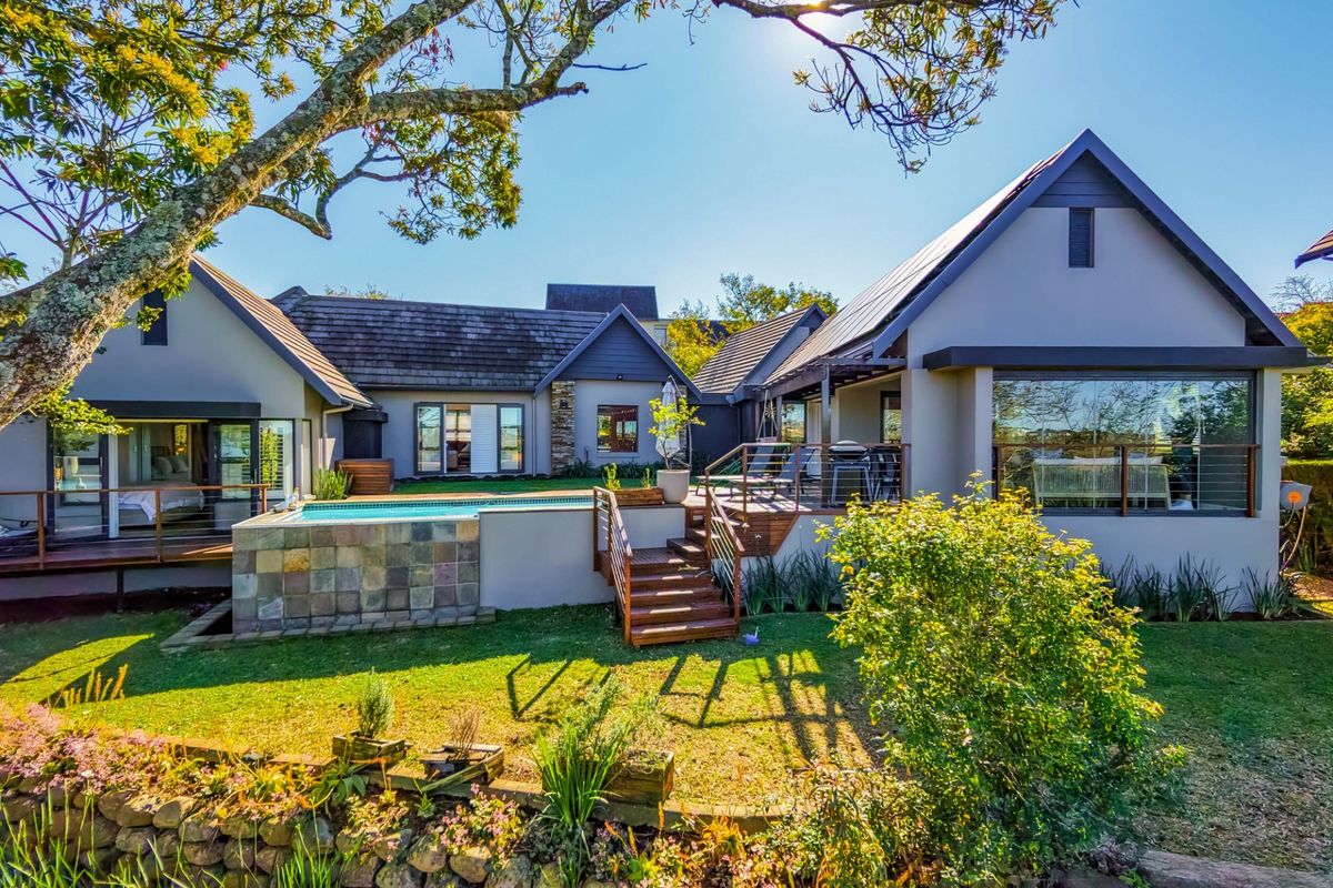Rear view of the property featuring a raised timber deck, swimming pool with stone cladding, and landscaped garden with a stone retaining wall.