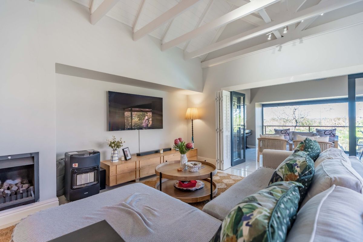 Spacious living room featuring a vaulted ceiling with exposed rafters, a built-in fireplace, and bi-fold doors leading to an outdoor balcony area.
