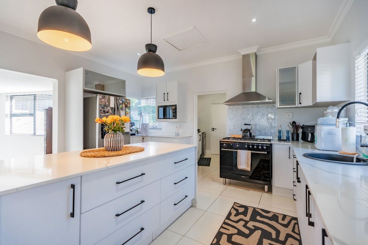Modern kitchen featuring a central island with quartz countertops, herringbone backsplash, gas stove, and sleek white cabinetry with black hardware.