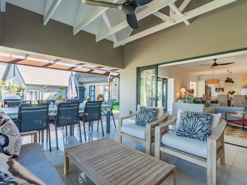 Spacious covered patio featuring exposed timber rafters, ceiling fan, and tiled flooring, seamlessly connecting to the interior living area through large sliding glass doors.