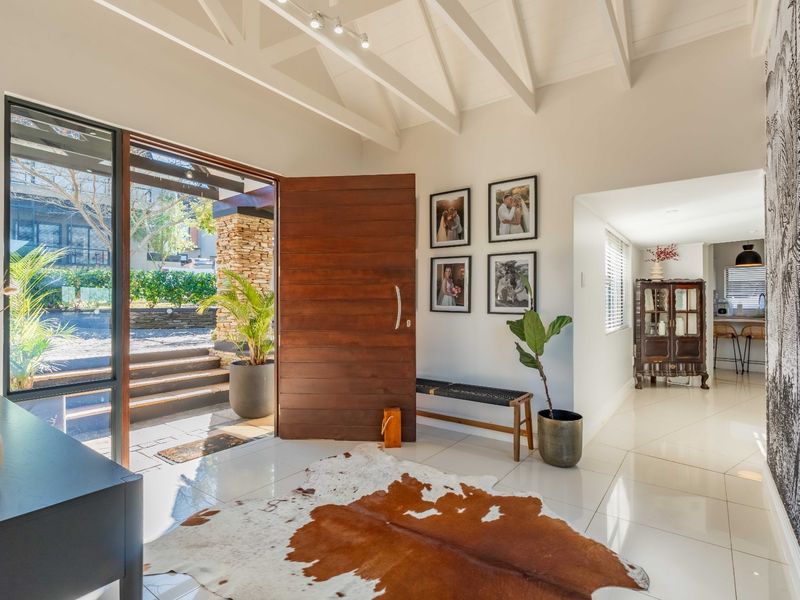 Bright and welcoming entrance hall featuring high ceilings with exposed timber beams, polished tiled flooring, and a large timber pivot door opening to the exterior.