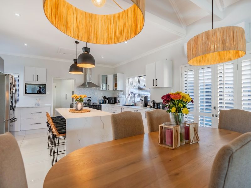 A bright open-plan kitchen and dining area featuring a large stone-topped island, modern cabinetry, vaulted ceilings, and plantation shutters.